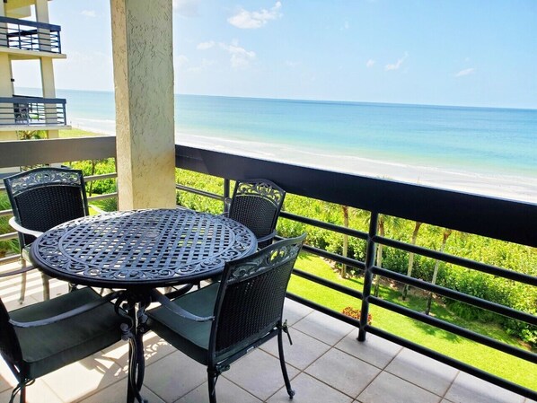 Ein Balkon mit rundem Tisch und Stühlen mit Blick auf einen Strand.