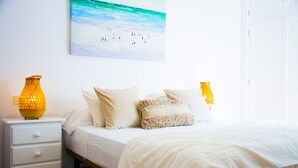 A bedroom with a bed, a nightstand, a lamp, and a painting on the wall. - Asana Surf House (Famara)