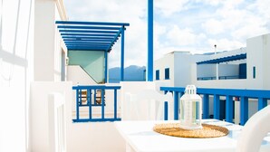 A white and blue outdoor seating area with a table and chairs, a lantern, and a view of the sea and mountains in the background. - Asana Surf House (Famara)