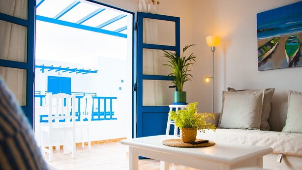 A bright living room with a white sofa, a small table with a plant, and a painting on the wall. - Asana Surf House (Famara)