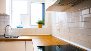 A kitchen with white cabinets, a wooden countertop, a stainless steel sink, and a window with a view of a building outside. - Asana Surf House (Famara)