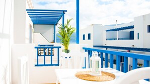 A balcony with white and blue furniture, a potted plant, and a table with a woven placemat. - Asana Surf House (Famara)