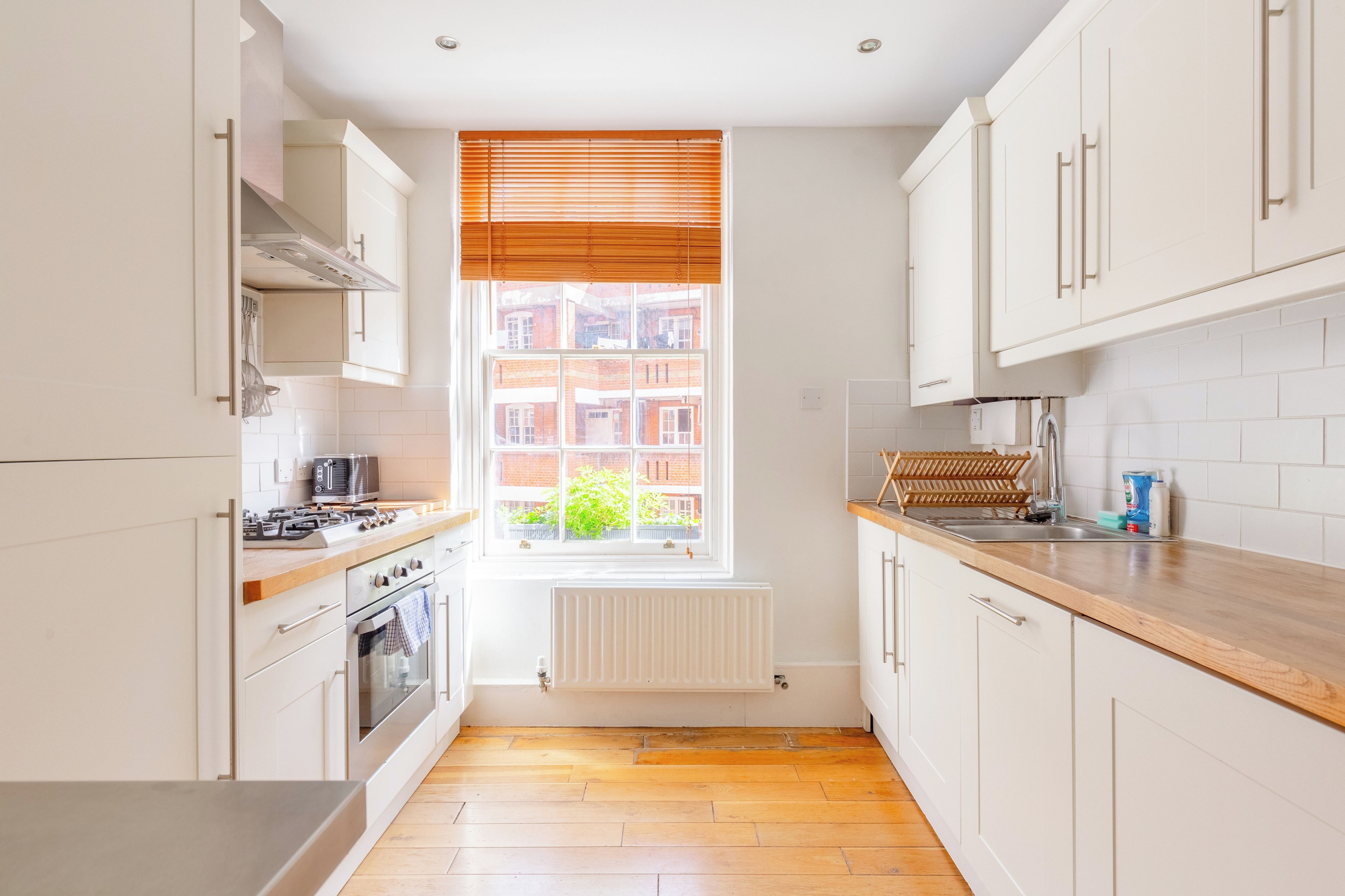 A modern kitchen with white cabinetry, a wooden countertop, a built-in oven, and a window with blinds.