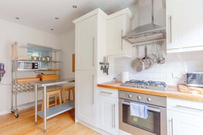 A modern kitchen with white cabinets, a stainless steel range, and a wooden countertop.