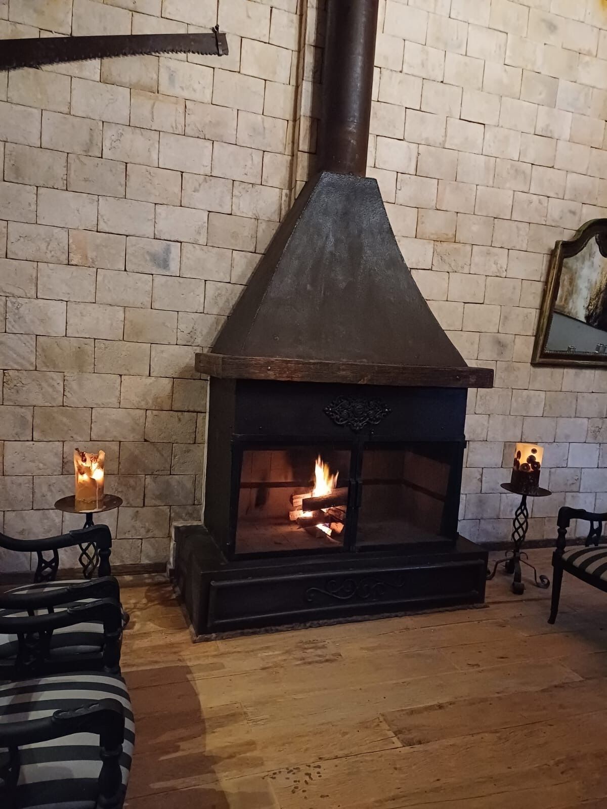 A stone fireplace with a chimney, a wooden bench, and a table with candles.