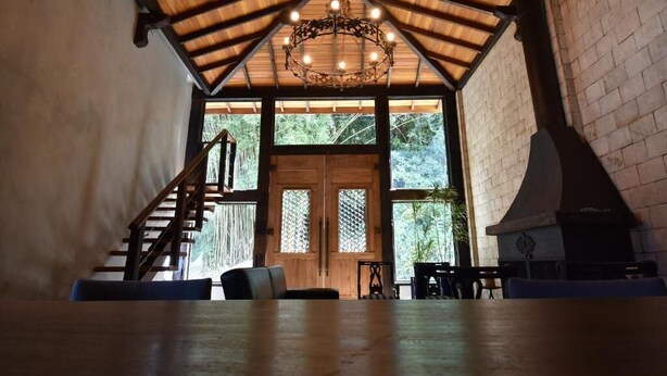 A rustic interior with a wooden ceiling, a chandelier, a fireplace, and a staircase leading to a balcony. - Pousada Villa Manso (Lima Duarte)