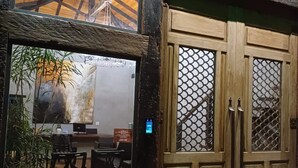 A wooden door with a mesh screen, a stone wall, and a view of a dining area with chairs and a table. - Pousada Villa Manso (Lima Duarte)