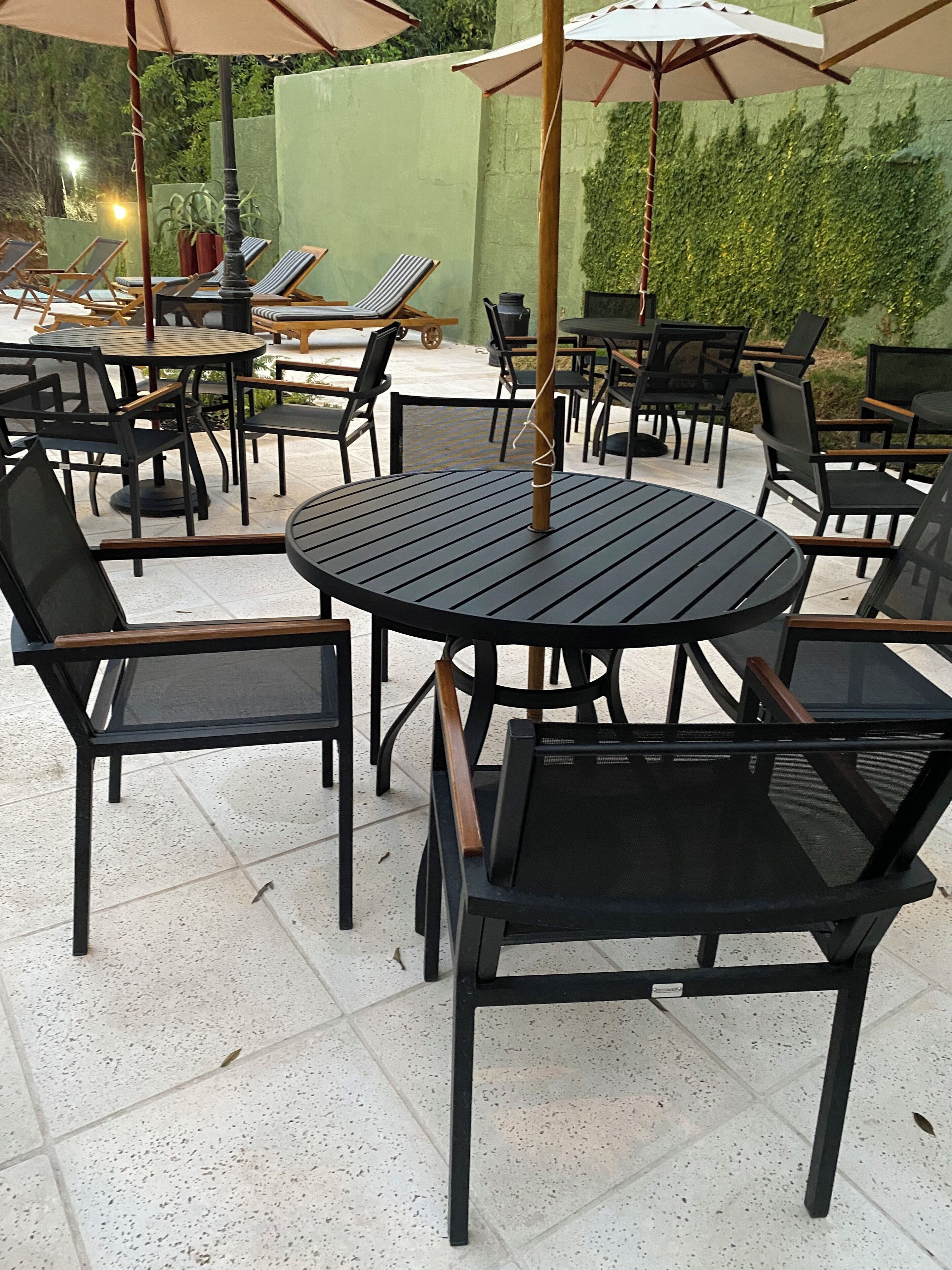 Un'area patio all'aperto con tavoli rotondi e sedie nere, ombreggiata da ombrelloni.