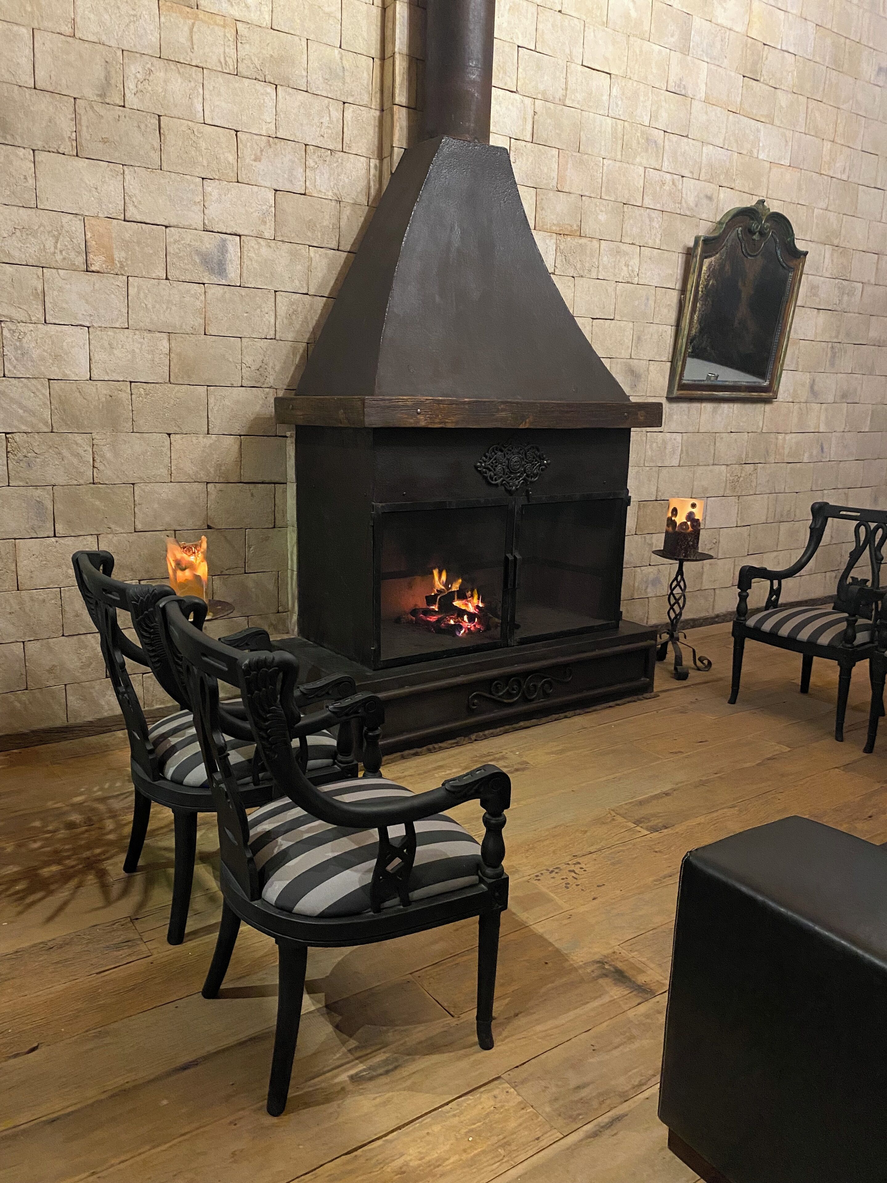 A cozy room with a stone wall, a black fireplace, and two upholstered chairs.
