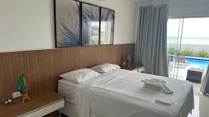 A hotel room with a bed, bedside tables, a wall-mounted air conditioner, and a view of the ocean through large windows.
