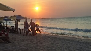 A beach scene with a sunset, umbrellas, and people.