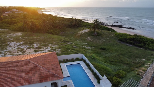 A residential property with a swimming pool, a red-tiled roof, and a view of the ocean.