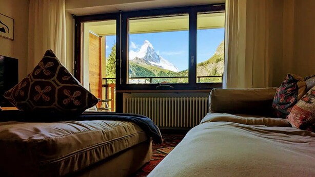 Habitación de hotel con cama, sofá y ventana con vistas a la montaña.