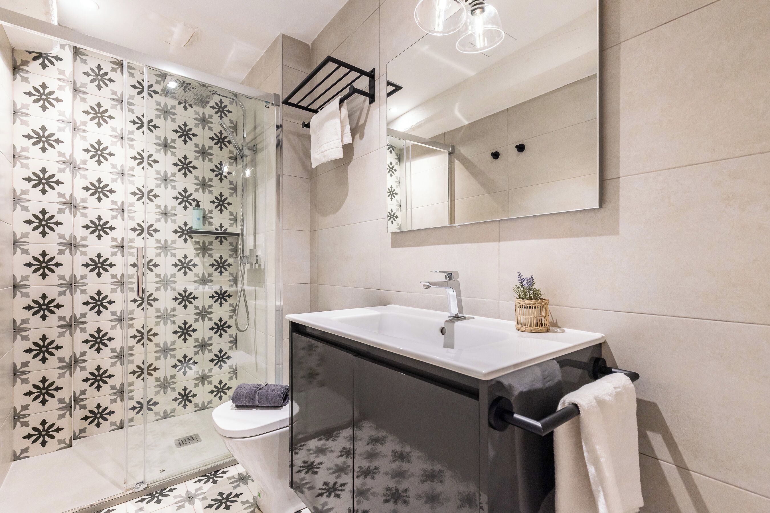 A modern bathroom with a glass shower enclosure, a white sink, and a large mirror.