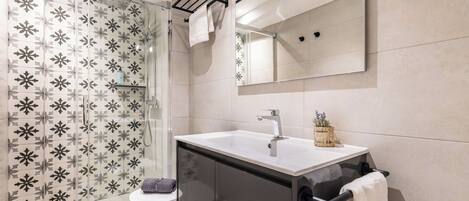 A modern bathroom with a glass shower enclosure, a white sink, and a large mirror.