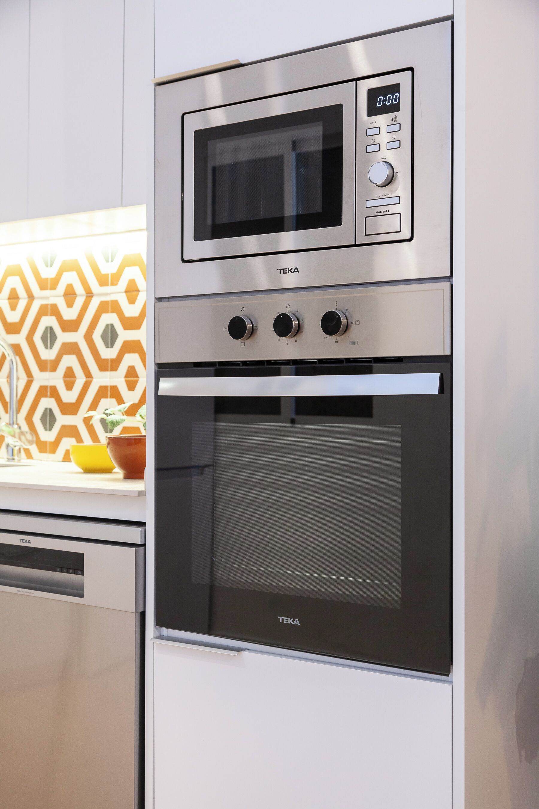 A kitchen with a built-in microwave and oven, a dishwasher, and a patterned backsplash.