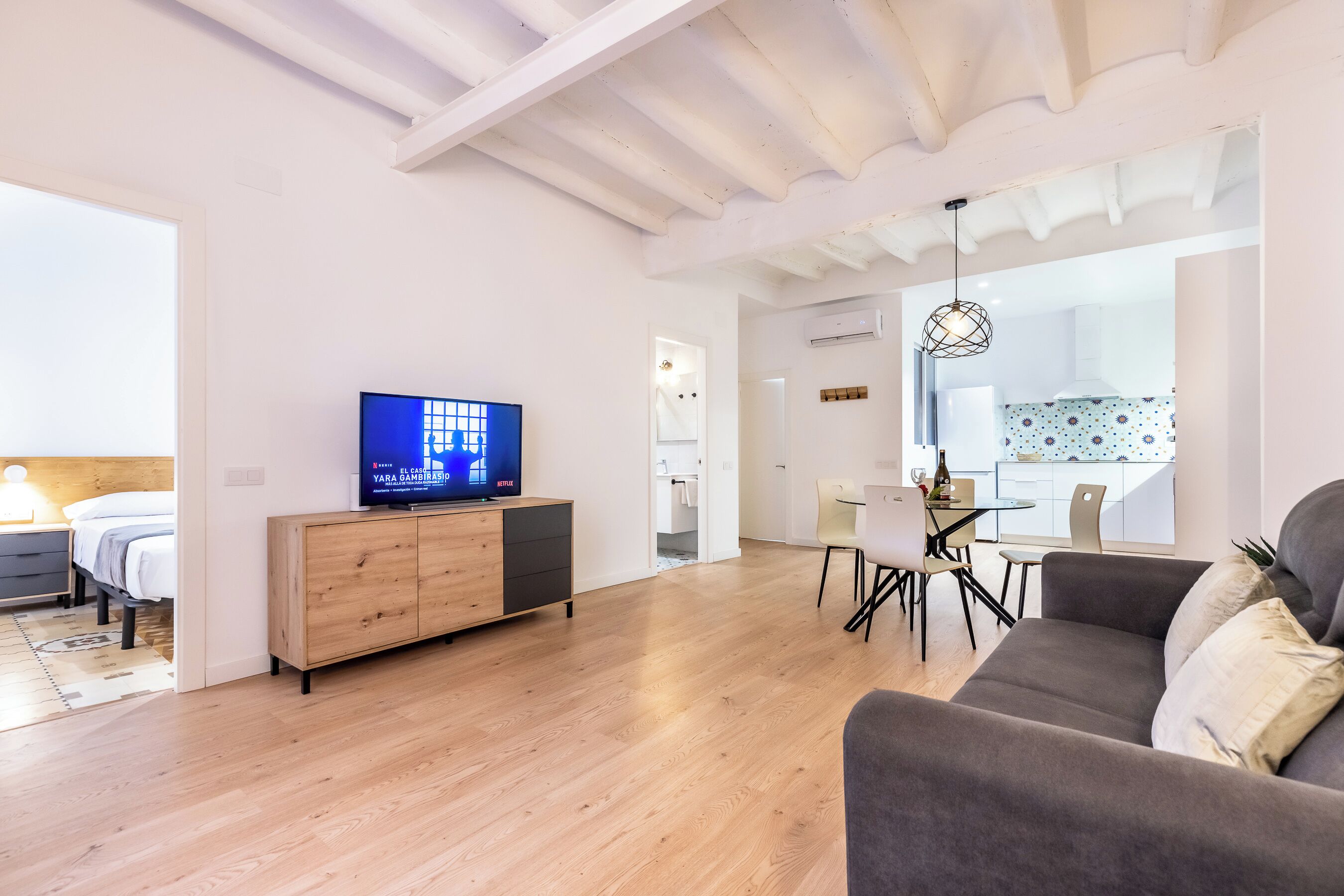 A modern living room with a TV, wooden cabinet, grey sofa, and a dining area with a table and chairs.