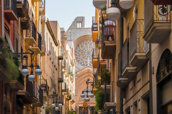 Une rue étroite bordée d’immeubles à plusieurs étages, agrémentée de balcons, de lampadaires et d’une fenêtre décorative particulièrement remarquable.