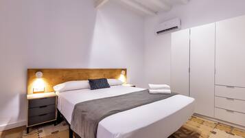 A neatly made bed with a wooden headboard, a bedside table with a lamp, and a wardrobe in a well-lit room.