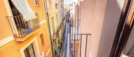 A narrow alleyway between buildings with balconies, a visible window, and a door.