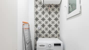 A compact laundry room with a Bosch washing machine, a drying rack, and a Bosch Thermostatic Air Conditioner mounted on the wall.