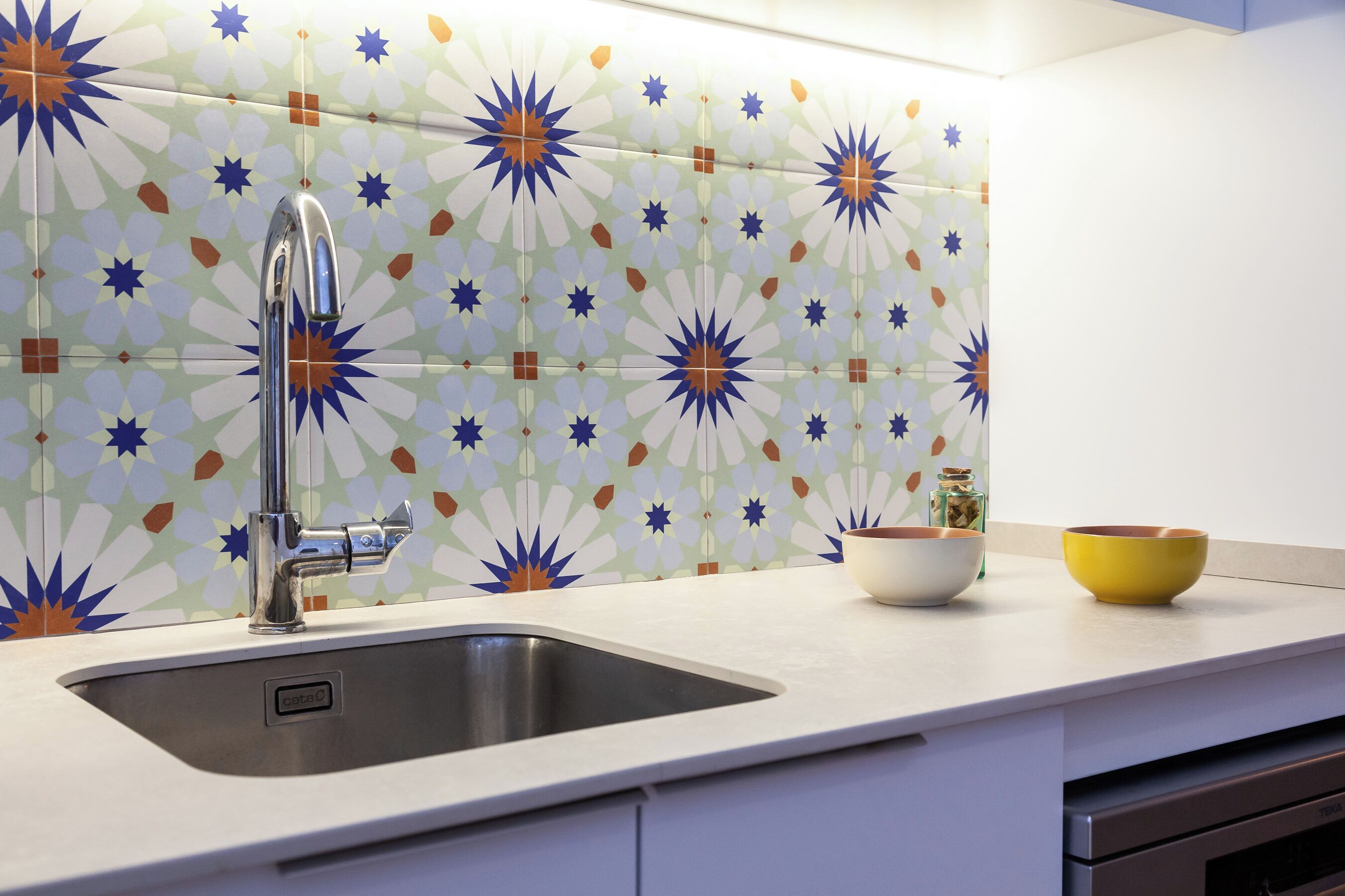 Una cocina con un lavamanos de acero inoxidable, armarios blancos y un salpicadero con diseño.
