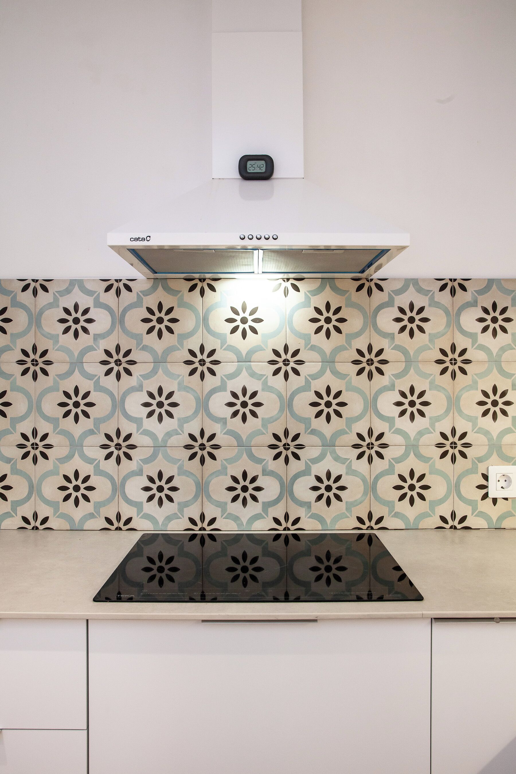 A kitchen with patterned tiles, a stove, and a digital clock.