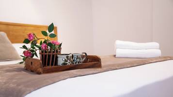 A neatly made bed with a brown bedspread, a wooden tray holding a camera and pink flowers, and a white pillow in a hotel room.