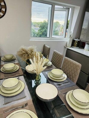 A dining area with a glass table set for four, beige chairs, and a vase with dried plants. - Stylish Two-story London Retreat (London)