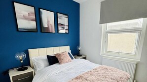 Une chambre à coucher avec un lit, des tables de chevet, une fenêtre et des œuvres d’art accrochées au mur.