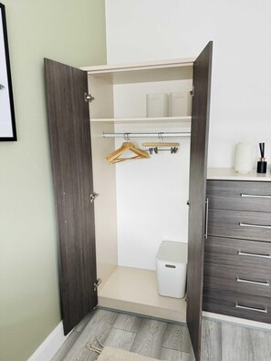 A walk-in closet with a wooden door, a hanging rod, shelves, and a small white trash bin. - Stylish Two-story London Retreat (London)
