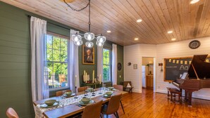A dining room with a wooden table set for six, a piano, and a large window with curtains. - 1880s Schoolhouse/Hot Tub/Firepit/Hocking Hills (McArthur)