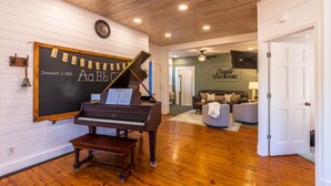 A piano, a chalkboard with a date, and a sign for 'Drakste Schoolhouse' in a room with wooden floors and white walls. - 1880s Schoolhouse/Hot Tub/Firepit/Hocking Hills (McArthur)