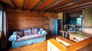A cozy cabin interior with a plaid sofa, wooden dining table, and a kitchen area.