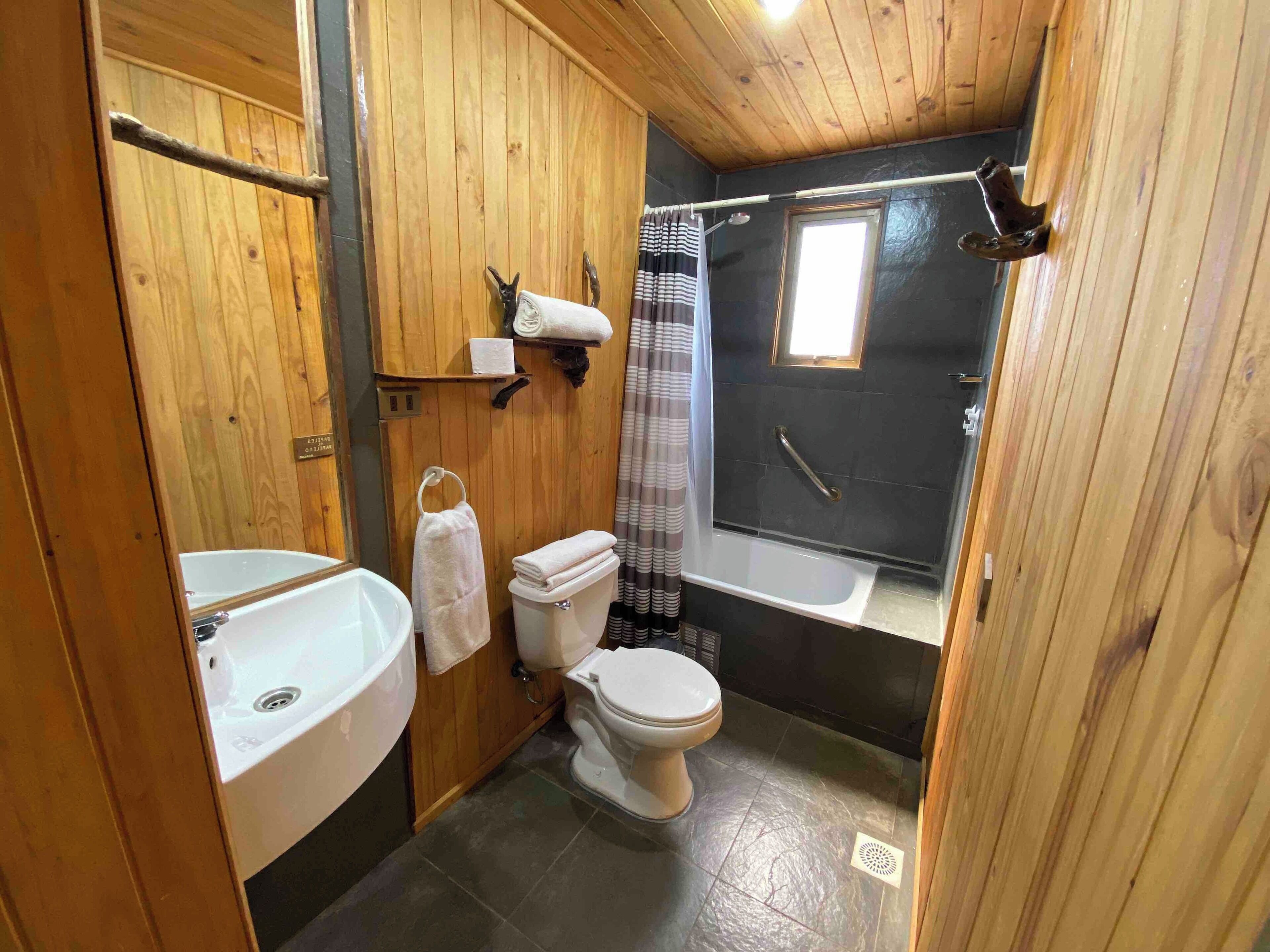 A compact wooden bathroom with a sink, toilet, and shower.