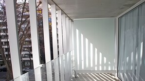 En moderne balkon med gelænder af glas, udsigt over bybilledet og et mønstret gulv.