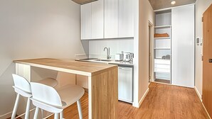A compact kitchen with white cabinets, a wooden countertop, and a built-in dishwasher. There are two white chairs at a small table. - 802 Very bright studio apartment in Belgrano (CABA)