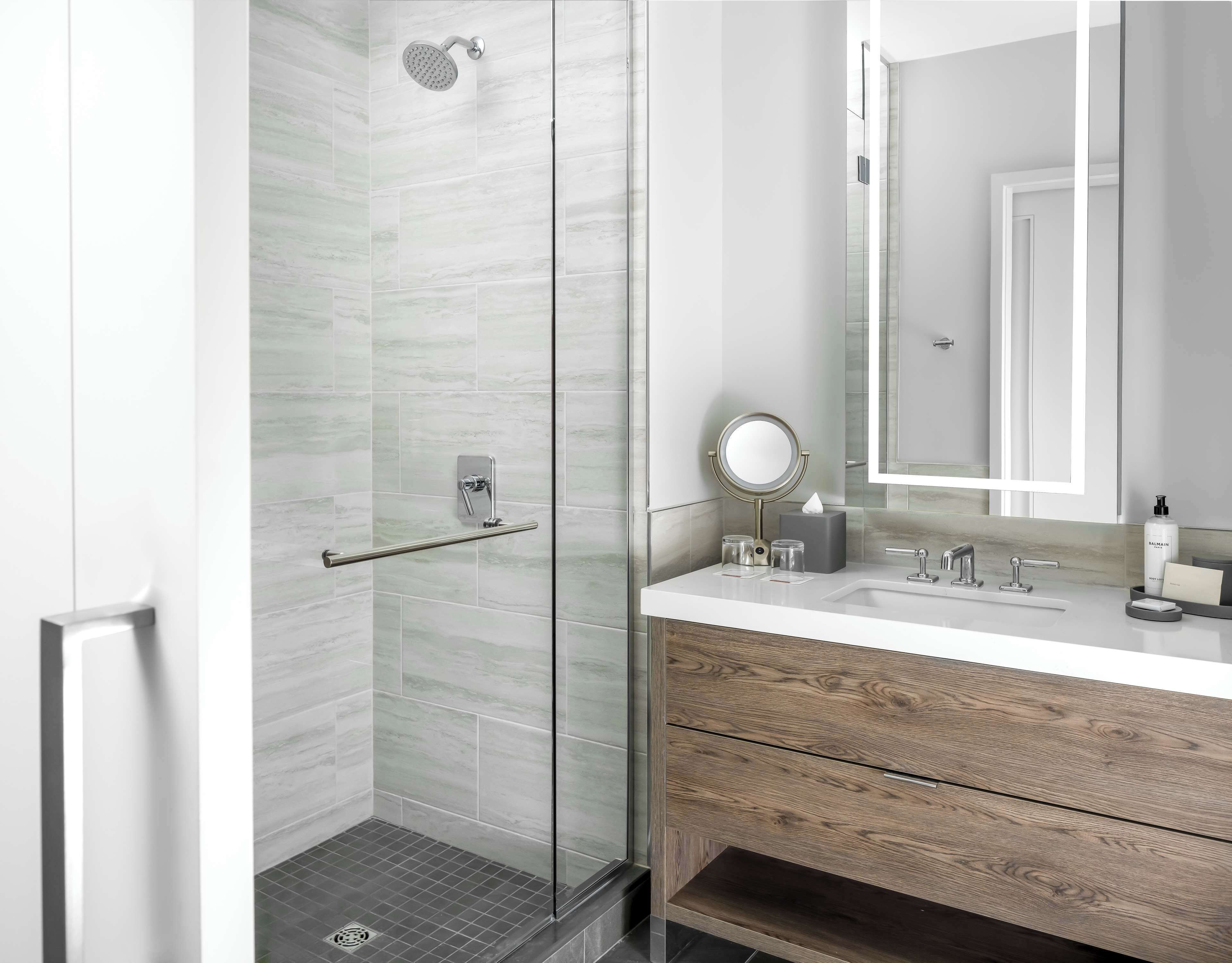 Un baño moderno con cabina de ducha de vidrio, tocador con espejo y armario de madera.