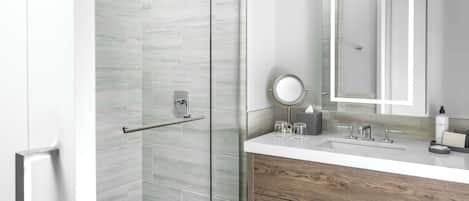 Un baño moderno con cabina de ducha de vidrio, tocador con espejo y armario de madera.