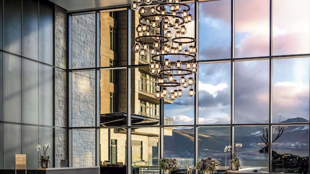 A modern hotel lobby with a large glass wall, a chandelier, and a reception desk.