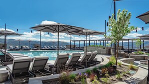 A poolside area with lounge chairs and umbrellas, a pool, and a view of mountains.