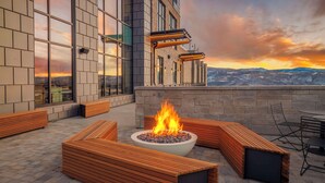 A rooftop patio with a fire feature, seating, and a view of the cityscape during sunset.