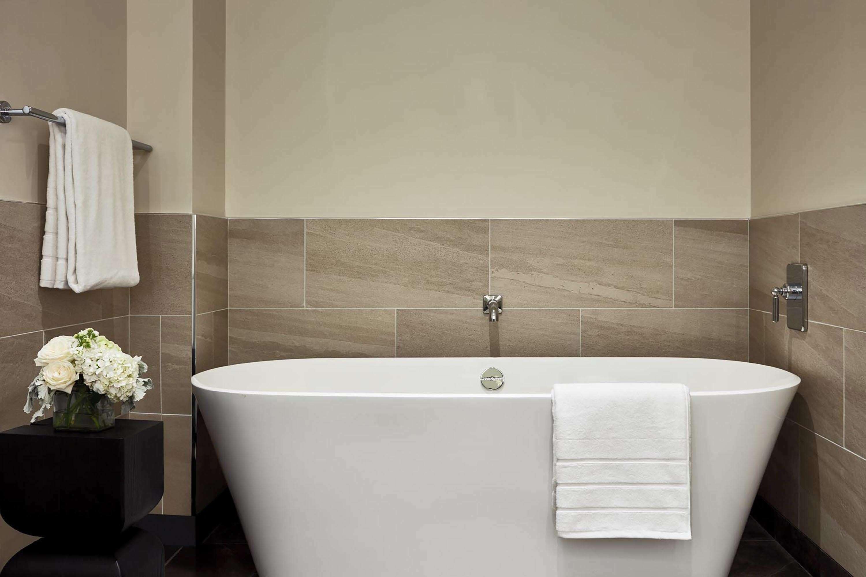 A modern bathroom with a freestanding bathtub, a black pedestal sink, and a vase of white flowers.