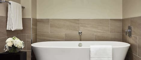 A modern bathroom with a freestanding bathtub, a black pedestal sink, and a vase of white flowers.