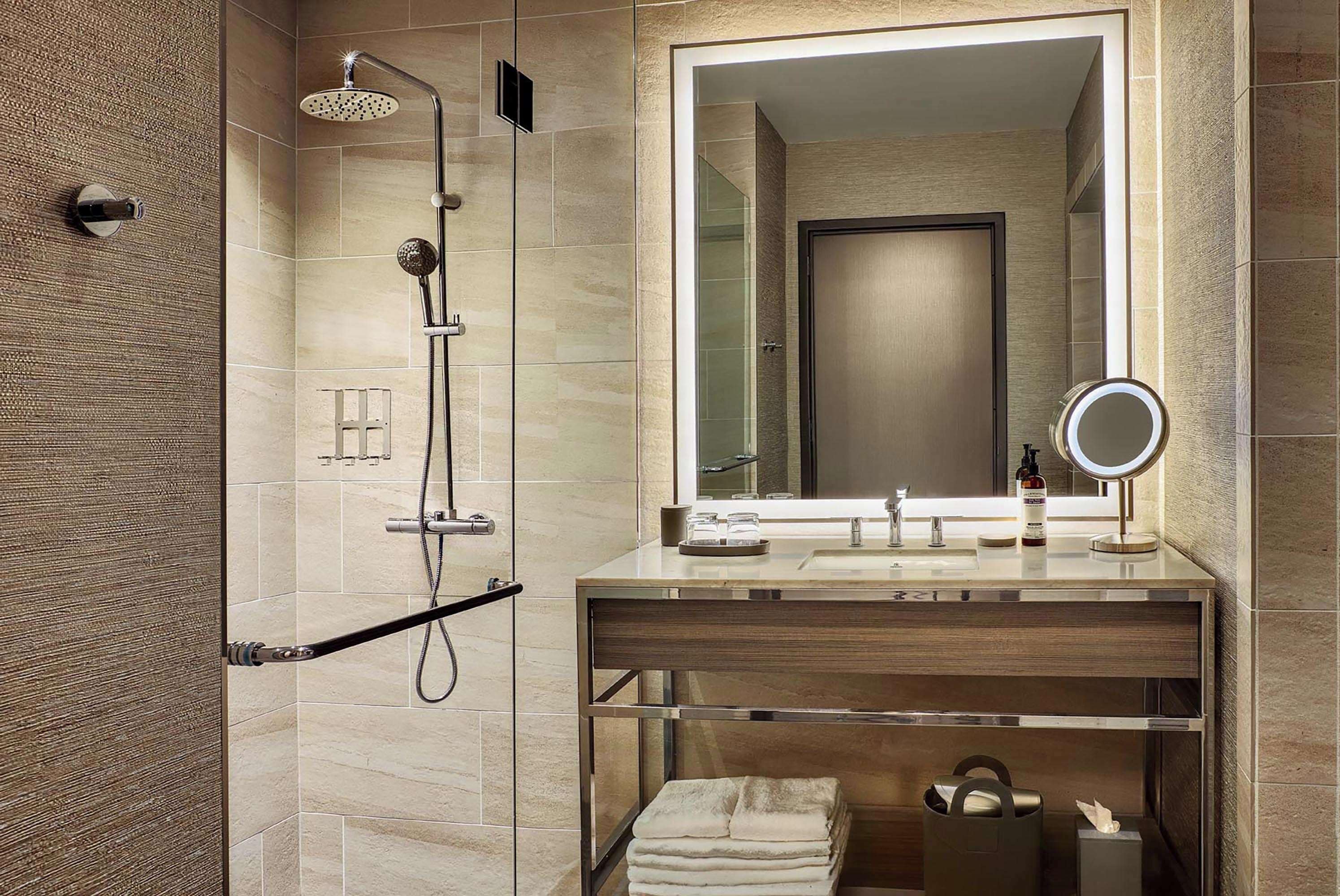 A modern bathroom with a shower, a large mirror, and a vanity with a towel rack.