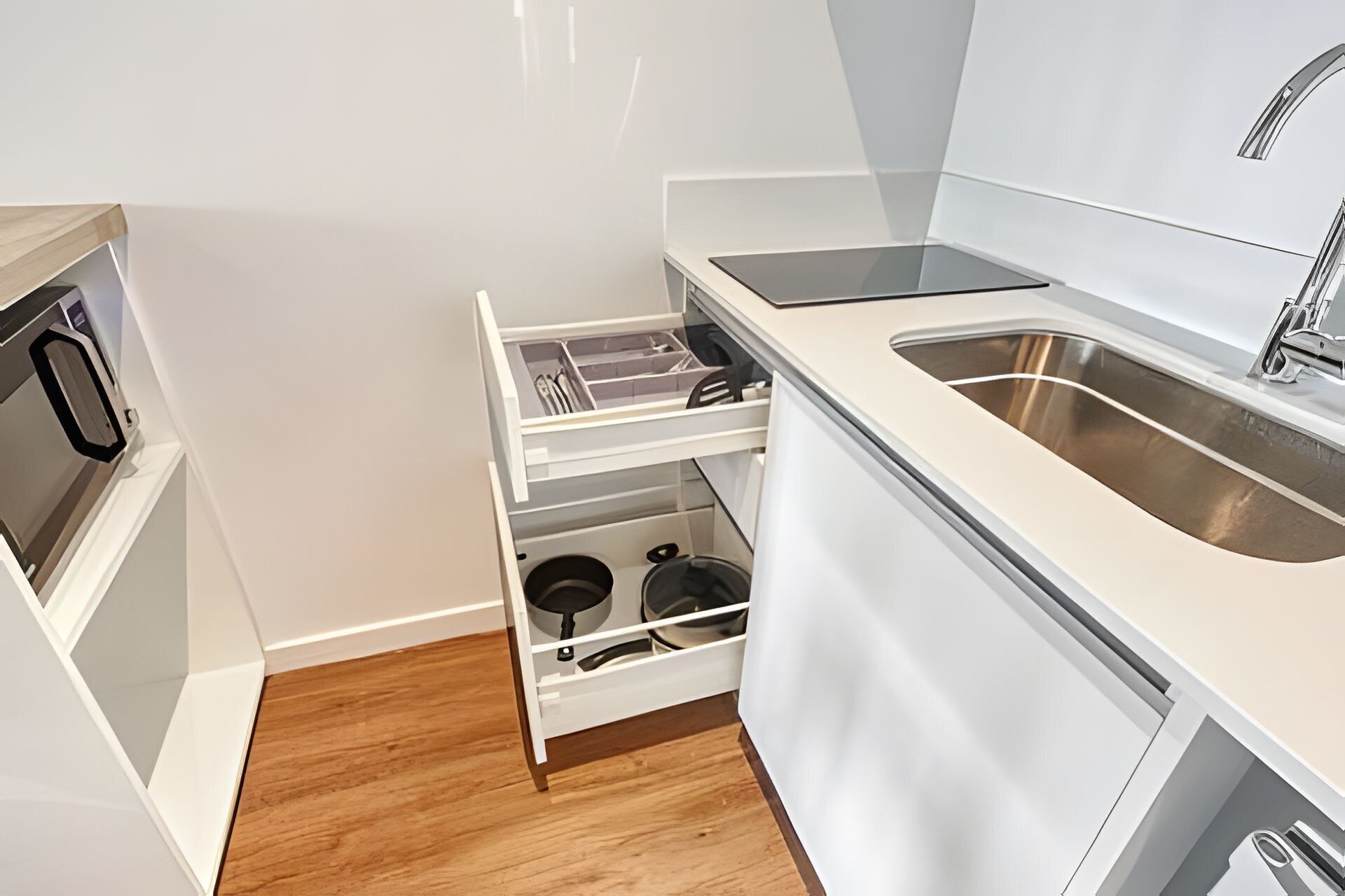 A compact kitchen with white cabinetry, a built-in oven, a sink, and a wooden floor.