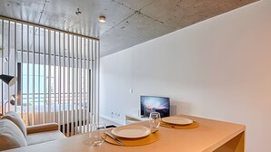 A modern dining area with a wooden table, two plates, and a glass. A TV is mounted on the wall, and a window with blinds is visible. - 504 Monoambiente moderno en Belgrano (CABA)