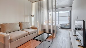 A modern living room with a sofa, a coffee table, and a view through a window with vertical blinds. - 504 Monoambiente moderno en Belgrano (CABA)
