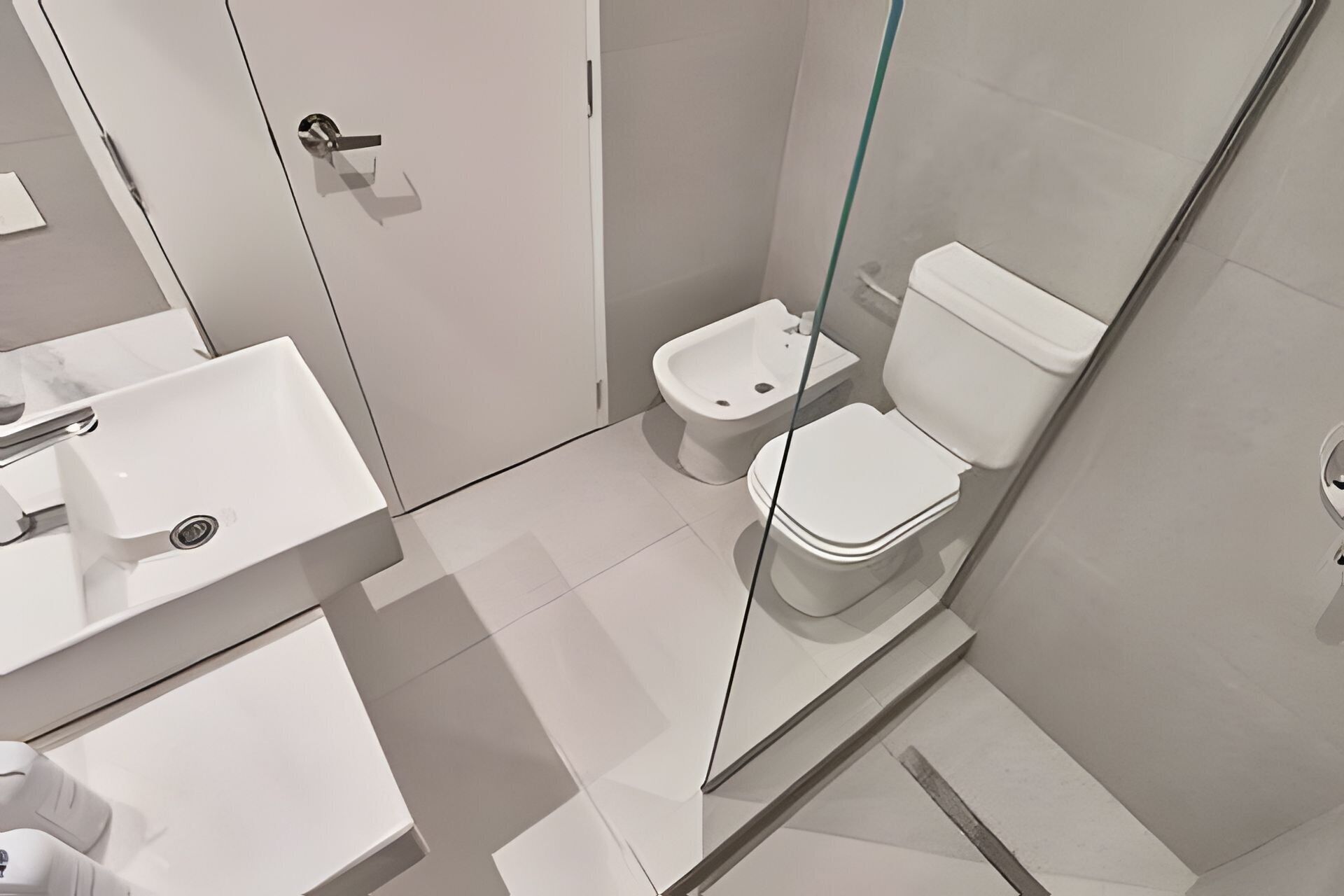 Un baño moderno con cabina de ducha de vidrio, inodoro blanco y lavamanos.