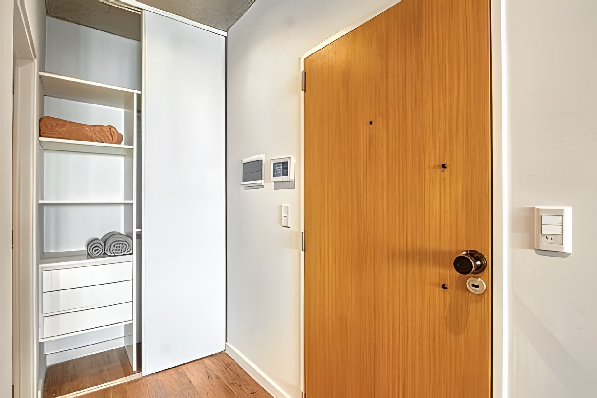 Una habitación con puerta de madera, paredes blancas y un armario empotrado con estantes y barra para colgar.